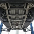 Inspector pointing at A-pillar joint area with car door fully open, checking for repair welds, bright outdoor Dubai setting