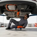 Inspector under lifted EV checking orange high-voltage cable routing and battery casing condition, gloves rated for HV, bright outdoor Dubai daylight