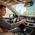 Inspector standing beside car waving hand past side mirror checking blind spot light flash, orange indicator lit, bright Dubai outdoor afternoon