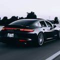 Inspector pressing brake and gas pedals checking feel, foot on pedal, seatbelt buckled, bright interior with Dubai visible through windshield