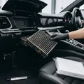 Inspector pulling cabin air filter from behind open glove box, dirty filter visible in hand, clean replacement filter on passenger seat, bright interior light