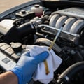 Close-up of inspector wiping dipstick on white cloth checking oil color and level, golden oil streak on fabric, engine bay in bright outdoor Dubai light