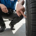 Inspector crouching reading DOT date code on tire sidewall, finger pointing at four-digit number, bright natural daylight on rubber surface