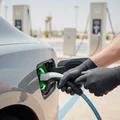 Inspector opening charge port flap on car fender, plugging Type 2 connector in, green LED ring activating, bright outdoor Dubai charging station