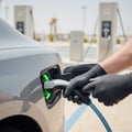 Inspector opening charge port flap on car fender, plugging Type 2 connector in, green LED ring activating, bright outdoor Dubai charging station