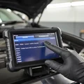 Close-up of scanner screen displaying fault code list P0301 P0420, engine and transmission tabs visible, inspector's gloved thumb scrolling results, bright interior
