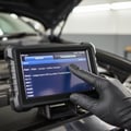 Close-up of scanner screen displaying fault code list P0301 P0420, engine and transmission tabs visible, inspector's gloved thumb scrolling results, bright interior