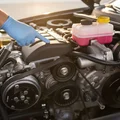 Inspector standing over engine bay pointing at each fluid reservoir, yellow oil cap, pink coolant tank, clear brake fluid bottle all visible, Dubai morning sun lighting everything