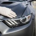 Close-up of inspector's gloved hand wiping headlight lens, LED elements visible inside housing, bright Dubai outdoor light