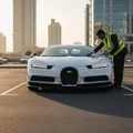Inspector standing in front of SUV checking both headlights are on, DRL strip glowing, Dubai parking lot, late afternoon sun casting long shadows