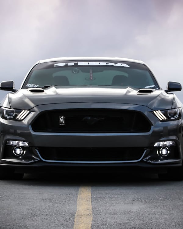 Inspector holding digital paint thickness gauge pressed flat against white SUV hood, close-up showing gauge display reading 120 microns, car parked outdoors in bright Dubai sunlight
