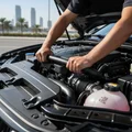 Inspector squeezing upper radiator hose with both hands testing pressure, engine warm and running, steam-free connections, bright Dubai outdoor engine bay