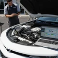 Silver SUV in bright Dubai sunlight, inspector checking panel gaps with diagnostic device