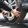 Close-up of inspector grabbing tire at 3 and 9 o'clock shaking for steering rack play, wheel off ground, bright outdoor Dubai daylight