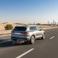 Rear three-quarter view of SUV accelerating on Dubai highway on-ramp, slight exhaust heat shimmer, bright sunny day, clear blue sky
