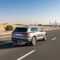 Rear three-quarter view of SUV accelerating on Dubai highway on-ramp, slight exhaust heat shimmer, bright sunny day, clear blue sky