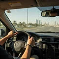 Inspector sitting in driver seat watching temperature gauge needle settle at 90, engine warmed up after test, Dubai road visible through windshield, bright afternoon
