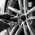 Close-up of inspector checking TPMS sensor valve stem, torque wrench on lug nut, alloy wheel rim surface visible, bright outdoor Dubai