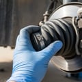 Inspector reaching under SUV center checking transfer case output seal for wetness, 4WD linkage visible, car on lift outdoor Dubai