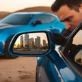 Inspector lifting trunk lid checking gas strut and latch mechanism, rubber seal visible around edge, Dubai parking lot, warm sunset light