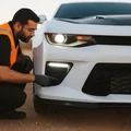 Inspector walking along car side checking turn signal blinking on front fender, orange flash reflecting on white paint, outdoor Dubai daylight