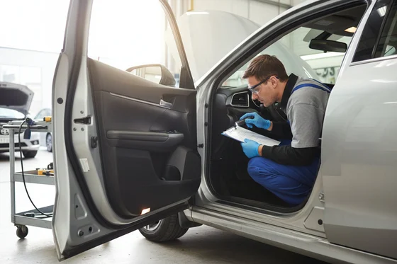 SUV raised on portable scissor lift outdoors, inspector underneath examining front frame rails with flashlight, bright Dubai daylight