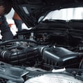 Close-up of inspector's flashlight aimed at water pump weep hole area, checking for coolant trail or stain, belt running beside it, bright engine bay light