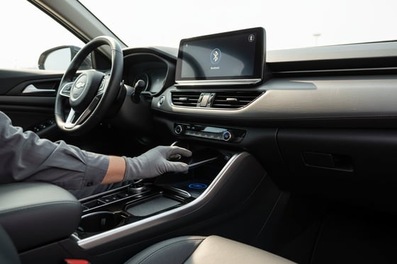 Inspector placing phone on wireless charging pad in center console, Bluetooth icon visible on touchscreen above, bright Dubai daylight through windows